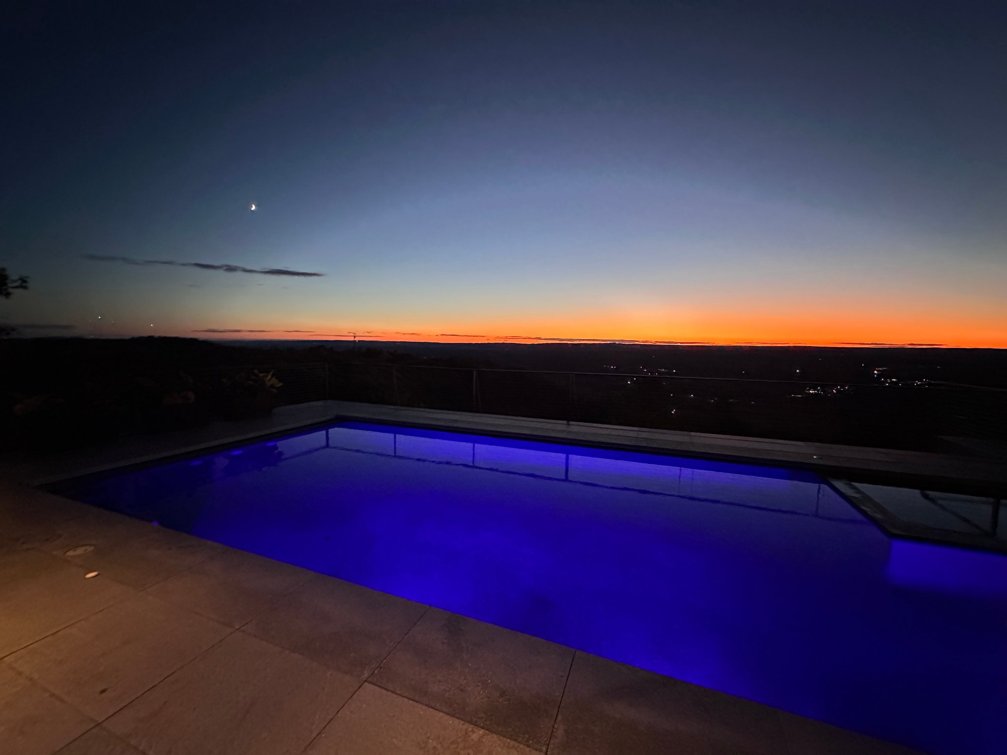 Beautifully illuminated pool at night with sunset sky